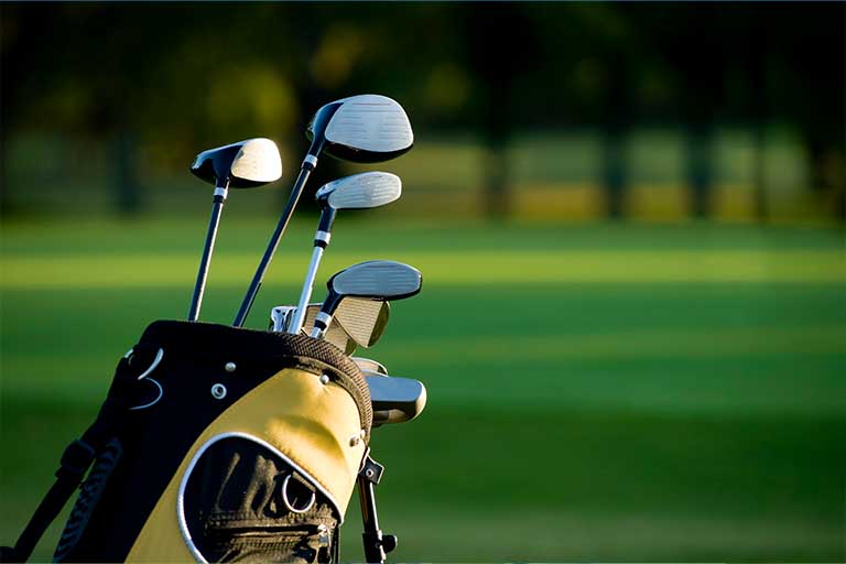 How to Choose the Right Golf Clubs for Your Game 2 A golf bag with clubs on a green course at sunset.