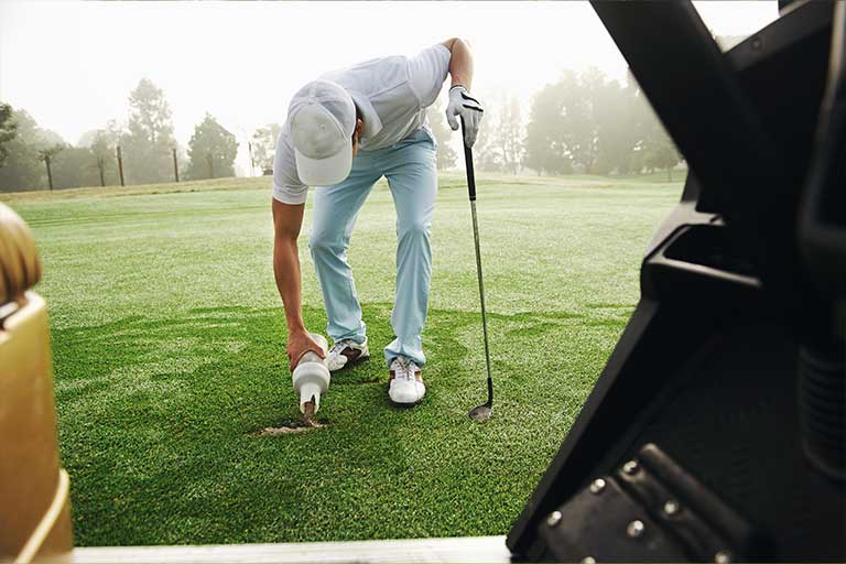 Golf Etiquette: 10 Encouraged Rules of the Game 2 Golfer practicing golf etiquette by repairing a divot on a foggy day, with a golf cart in the foreground.