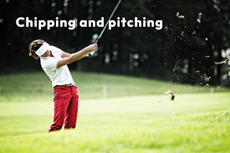A person wearing red pants and a white visor is playing golf, actively swinging a club on a grassy course. The text reads "Chipping and pitching.