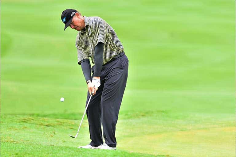 Chipping consistency: 3 drills to sharpen your touch around the green 1 A golfer in a striped shirt and dark pants watches the ball as he makes a shot on a grassy course. The golfer is working on chipping consistency.