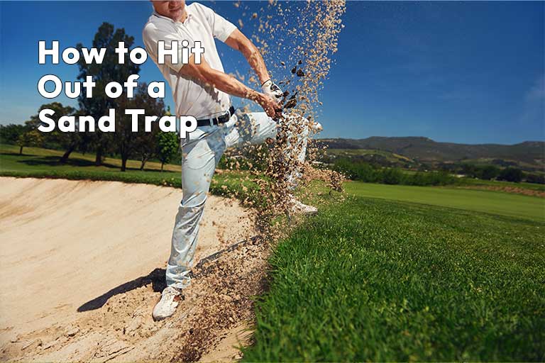 Golfer in white attire swinging at a golf ball in a sand trap, with sand flying around, text overlay "how to hit out of a sand trap" above a lush green course background.