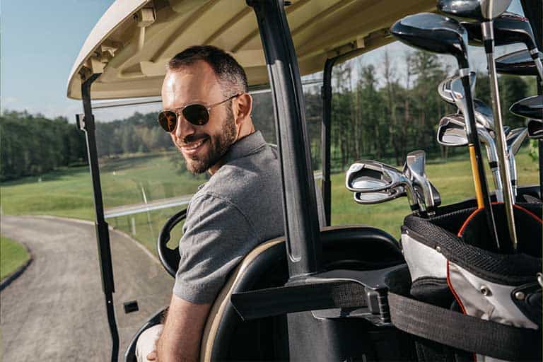Golf Cart Etiquette: 10 Do’s and Don’ts of Riding in a Golf Cart 1 Man with sunglasses smiling in a golf cart with clubs in the back.